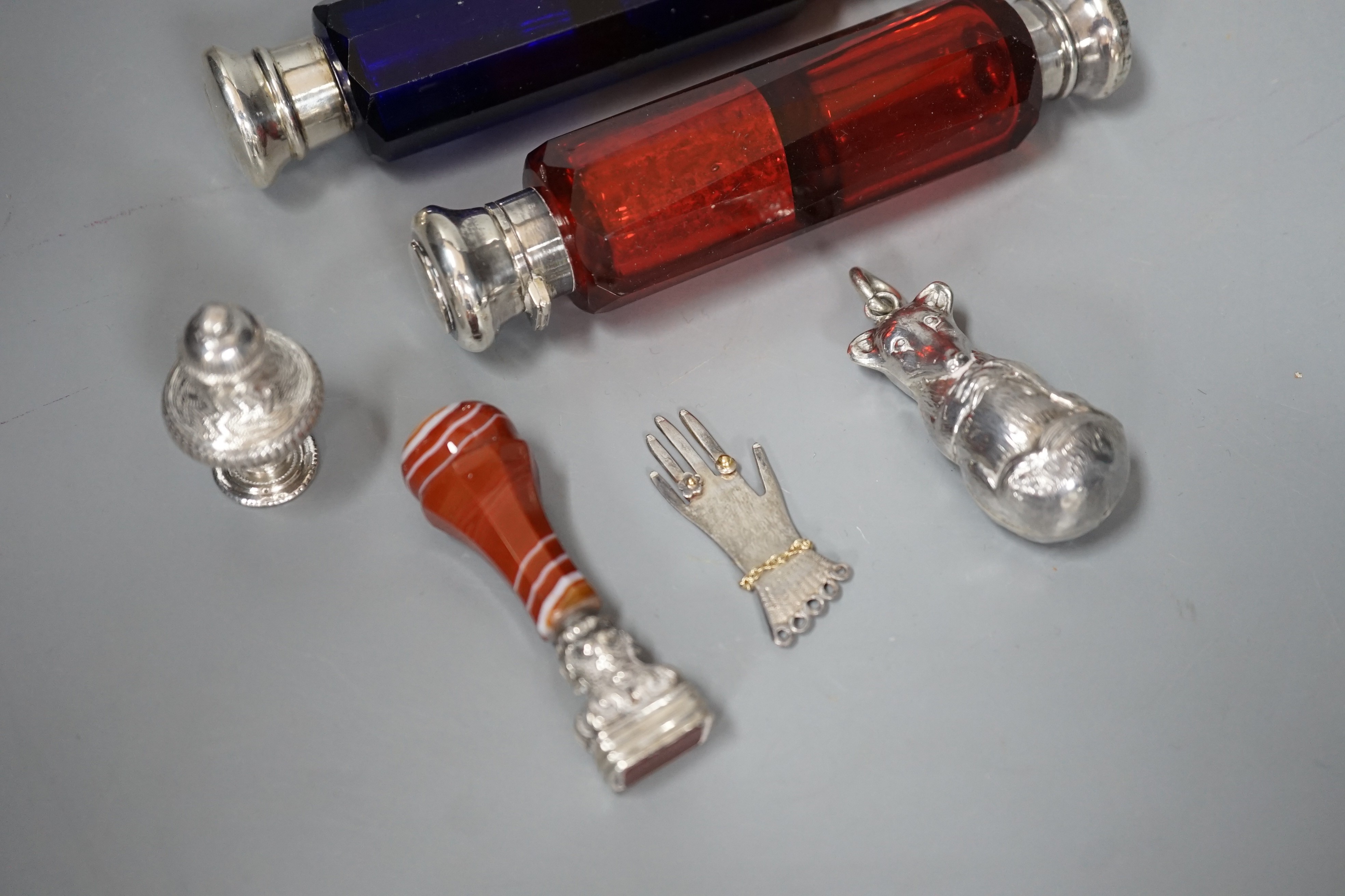 Two Victorian white metal mounted ruby or blue glass double ended scent bottles, 12.5cm, an agate mounted seal, a modern silver child's rattle, a continental scent/seal and a silver hand charm.